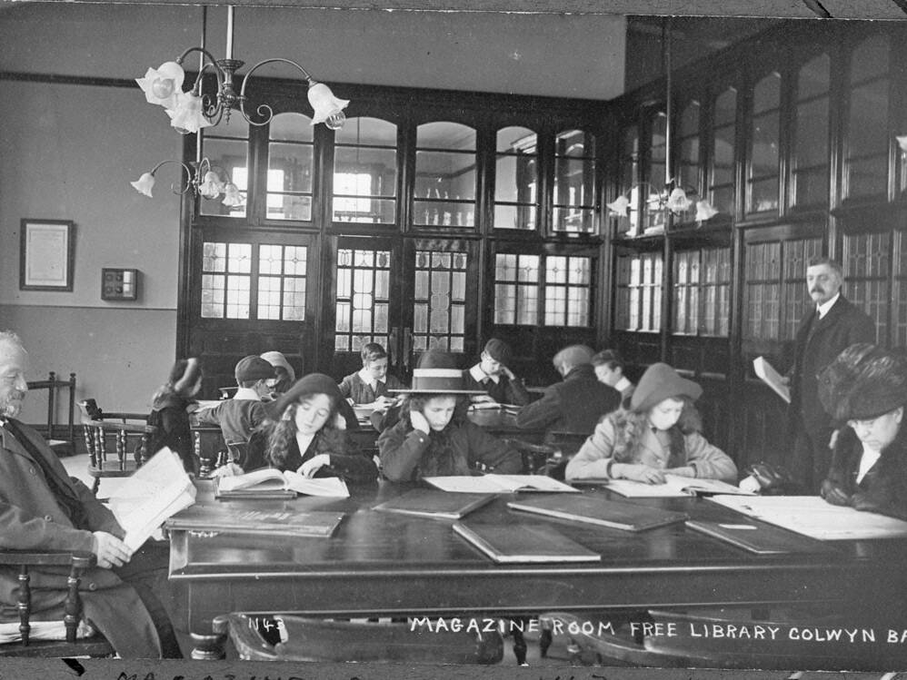 Black and white photo showcasing the interior of Colwyn Bay Library's Magazine Room with a group of children and three adults using the room.